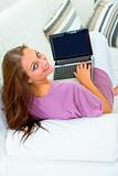 Smiling young woman sitting on sofa and using laptop
