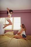 young adult women jumping for joy on bed