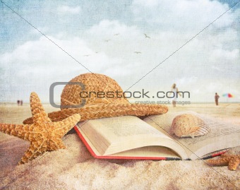Straw hat , book and seashells in the sand