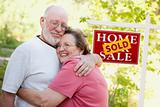 Happy Affectionate Senior Couple Hugging in Front of Sold Real Estate Sign.