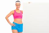 Smiling fitness young girl in sportswear holding blank billboard
