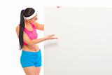 Fit girl in sportswear looking and pointing on blank billboard
