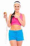 Smiling young fit girl pointing finger on apple with measuring tape
