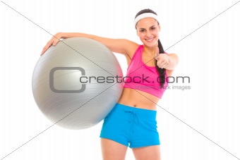 Smiling fit young girl with fitness ball showing thumbs up gesture
