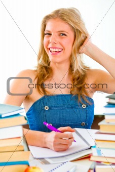 Smiling teen girl sitting at table with lots of books
