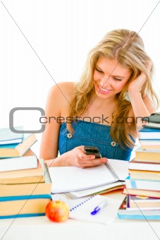 Smiling teen girl reading sms on mobile instead of doing homework
