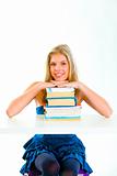 Smiling young girl sitting at desk and holding hands on piles of books
