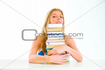 Sitting at table teen girl hugging pile of books and looking out
