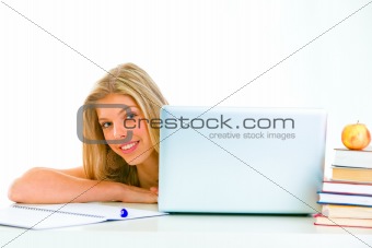Sitting at table smiling teen girl looking out from laptop
