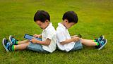 Two kids using touchscreen tablet PC on the grass