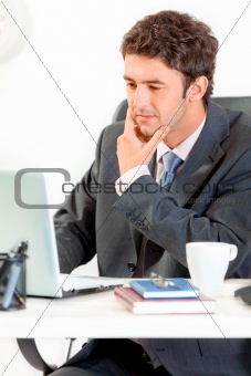 Thoughtful businessman sitting at office desk and working on laptop
