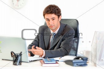 Modern businessman sitting at office desk and pointing finger on laptop
