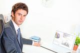 Serious businessman sitting at office desk with laptop
