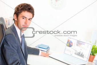 Serious businessman sitting at office desk with laptop
