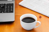 White cup of coffee with laptop and newspaper