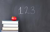 Stack of books with a red apple and a blackboard with "123" writ