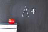 Stack of books with a red apple and a blackboard with "A+" writt