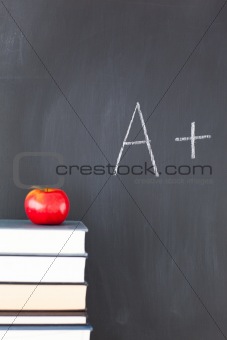 Stack of books with a red apple and a blackboard with "A+" writt