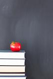 Stack of books with a red apple and a clean blackboard