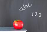 Stack of books with a red apple and a blackboard with figures an