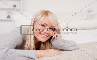 Attractive happy blond woman talking on cell phone lying down on