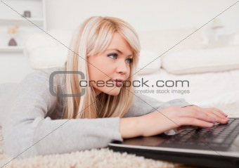 Beautiful concentrated woman relaxing on laptop lying on a carpe