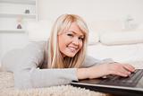 Beautiful blond woman relaxing on laptop lying on a carpet