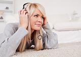 Beautiful blond woman with headphones lying on a carpet