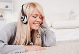 Prettyl blond woman with headphones lying on a carpet