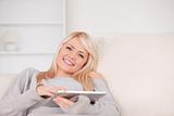Pretty blond woman lying on a sofa relaxing on a line of tablet 