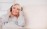 Beautiful blond woman with headphones lying in a sofa