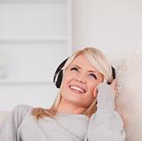 Pretty young blond woman with headphones lying in a sofa
