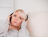 Attractive young blond woman with headphones lying in a sofa