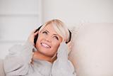 Charming young blond woman with headphones lying in a sofa