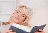 Concentrated blonde woman reading a book while lying on a sofa