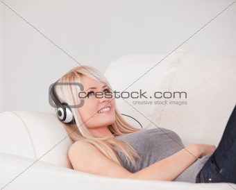 Happy young blond woman with headphones lying in a sofa