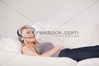 Smiling young blond woman with headphones lying in a sofa