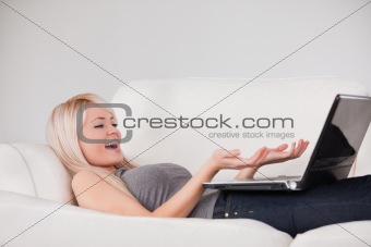 Joyful woman relaxing on laptop lying on a sofa