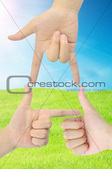 hand as triangle shape on fresh grass and blue sky