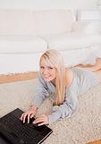 Beautiful young blond woman relaxing on laptop lying on a carpet