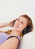 Cute blond-haired woman listening to music lying on the sofa