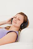 Happy blond-haired woman listening to music lying on the sofa