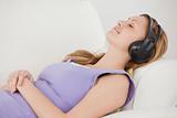 Delighted blond-haired woman listening to music lying on the sof