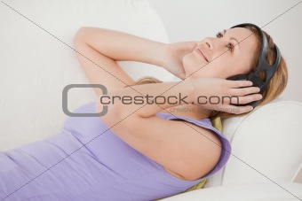 Relaxed blond-haired woman listening to music lying on the sofa