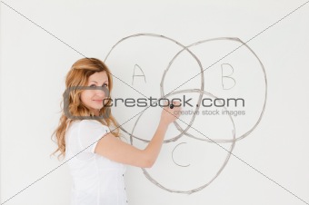 Blond-haired teacher looking at the camera while drawing a schem