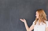 Attractive teacher showing an empty blackboard