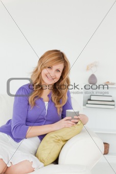 Smiling red-haired woman posing while sitting on a sofa