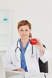 Cute female doctor showing a red apple to the camera in her surg