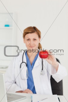 Cute female doctor showing a red apple to the camera in her surg