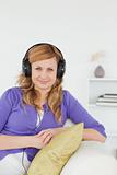 Pretty red-haired woman listening to music and posing while sitt